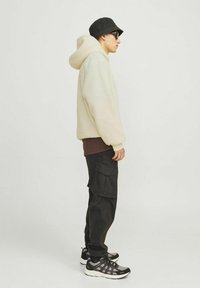 Fleece hoodie i off-white, med en stor hætte, parret med sorte cargo bukser. Accessories inkluderer en sort bucket hat og sneakers.