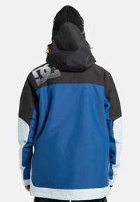 Niebieska i czarna kurtka z kapturem, z jasnoniebieskimi rękawami, z dużym logo na plecach i gładką teksturą materiału.