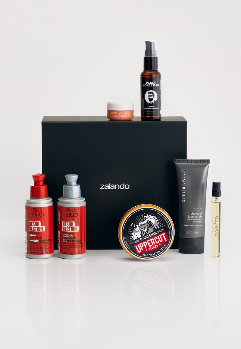 Eight grooming products arranged in front of a black box, featuring various colors and designs: two red bottles, a brown oil, a grey tube, and a gold tin.