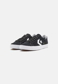 Schwarze Wildledersneaker mit einem weißen Sternlogo, kontrastierenden weißen Akzenten, flachen Schnürsenkeln und einer strukturierten weißen Gummisohle.