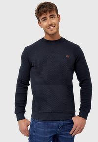 Navy sweater with a textured fabric design, crew neck, ribbed cuffs and hem, featuring a small brown logo patch on the chest.