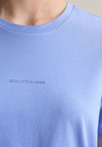 Jasnoniebieska bawełniana koszulka z okrągłym dekoltem, z małym szarym nadrukiem "Marc O'Polo DENIM" z przodu. Gładka tekstura.