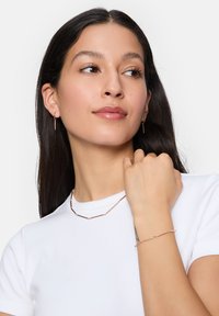 Rose gold jewelry featuring geometric bar designs in a necklace and matching bracelet, showcased with a white t-shirt.