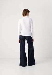 White long-sleeve top paired with dark blue wide-leg jeans. The top has a mock neckline; jeans feature back pockets with contrasting stitching.