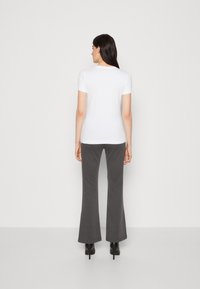 T-shirt bianco a maniche corte abbinato a pantaloni a zampa d'elefante grigi scuri e tacchi alti neri, che mostrano una silhouette liscia e aderente visto da dietro.