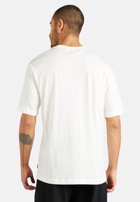 Hvid T-shirt med korte ærmer, fremstillet af blødt bomuld, har en klassisk rund halsudskæring og en afslappet pasform, med et lille logo-tag på siden.