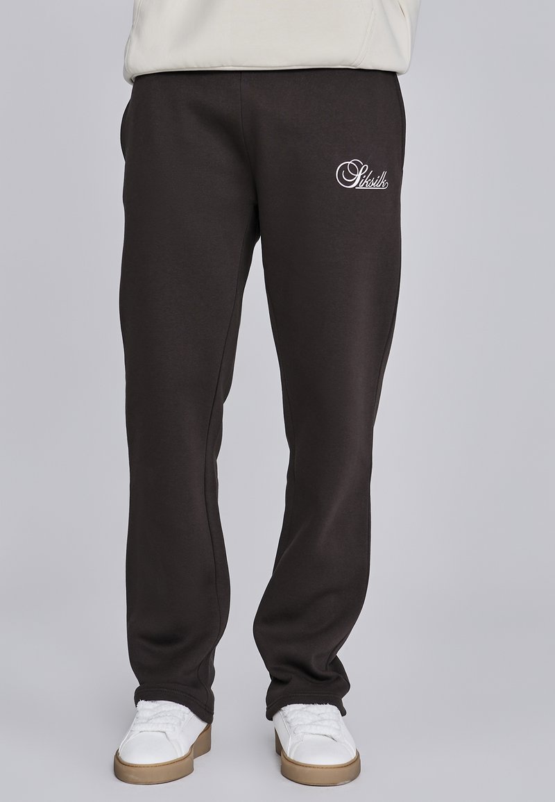 Zwarte sweatpants met geborduurd wit logo, elastische tailleband en taps toelopende broekspijpen. Zachte stof met een gladde textuur. Gecombineerd met witte sneakers.
