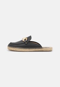 Scarpa nera in pelle slip-on con un accento dorato, caratterizzata da una suola intrecciata in juta e dettagli cuciti lungo il bordo.