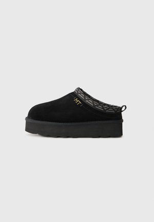 Black suede slip-on shoe with a patterned grey rim and a thick rubber sole. Features a pull tab and gold logo detail.