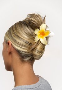 Håraccessoar med en stor, gul och vit blomdesign, gjord av glansigt material, fastklämd i en knutfrisyr. Mjuk, glänsande yta.