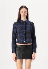 Mėlynos plaid švarkelis su mygtuk�ų uždarymu, dviem krūtinės kišenėmis ir ilgomis rankovėmis, derinamas su juoda odine mini sijonu.