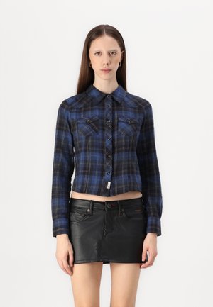 Blue plaid cropped shirt with button closure, two chest pockets, and long sleeves, paired with a black leather mini skirt.
