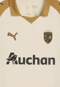 Jersey crema con detalles dorados, diseño de escote en V, que presenta un logo negro de Auchan, un logo dorado de Puma y un emblema conmemorativo del Racing Club de Lens.