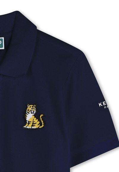 Marineblauwe polo met textuurstof, met een geborduurde gele en zwarte tijger op de voorkant en merktekst op de mouw.