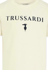 Kremowa bawełniana koszulka z krótkim rękawem, z nadrukowanym na czarno logo "TRUSSARDI" oraz sylwetką psa, z okrągłym dekoltem.