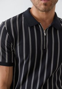 Polo shirt marine à manches courtes avec des rayures verticales blanches, présentant un col zippé et un tissu texturé.