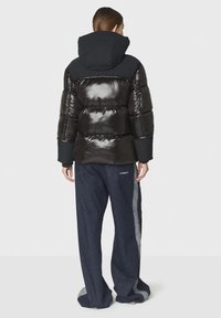 Giacca in piuma nera lucida con cappuccio e polsini a coste, abbinata a pantaloni in denim scuro con una striscia laterale grigia chiara e dettaglio del logo.