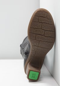 Black leather boot with textured sole, featuring a tread pattern and a green accent on the heel. Side zipper for easy wear.