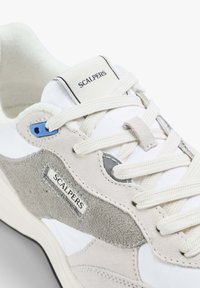 Sneaker bianchi e grigi con materiali in suede e tessuto, dotati di stringhe, un'accento blu e un'etichetta con logo ricamata sul lato.