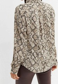 Långärmad blus i beige med ett ormtrycksmönster, i en texturerad tyg och med en rundad nederkant. Detaljerad med knäppta manschetter.