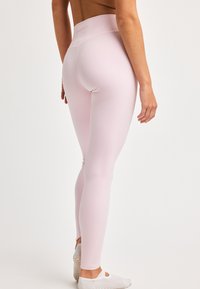 Lys rosa leggings laget av et glatt, elastisk materiale med høy midje. Inkluderer subtil merking på baksiden.