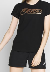 Camiseta negra con logo "asics" en bronce, mangas cortas y escote redondo, combinada con pantalones cortos deportivos negros.