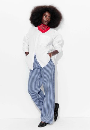 Chemise blanche à boutons avec des manches retroussées, pantalon rayé bleu et blanc, bandana rouge au cou, et ballerines noires à clous.