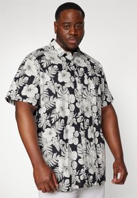 Camicia a maniche corte con sfondo nero, caratterizzata da grandi motivi floreali e foglie bianche, con bottoni frontali e vestibilità comoda.