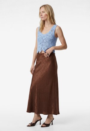 Vrouw draagt een lichtblauw mouwloos gehaakt topje, een bruine textuur lange rok en donkerbruine open-teen hoge hakken sandalen, staat zijwaarts.