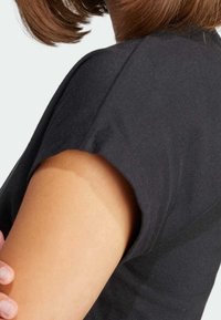 Black short-sleeve top with a rounded neckline and a relaxed fit, displaying a smooth cotton texture against bare skin.