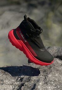 Schwarzer und roter Wanderschuh mit glatter Oberfläche, hohem Knöcheldesign, strukturiertem Seitenpanel und auffälligem Markenlogo.