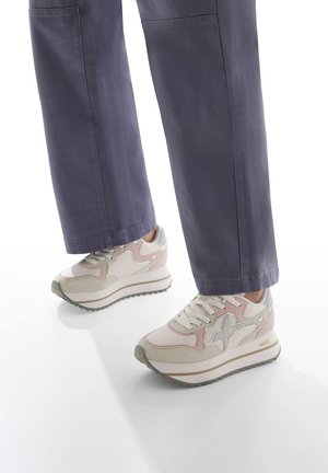 Sneakers in rosa chiaro e beige, con una parte superiore testurizzata, linguetta imbottita e una suola spessa e scanalata con accenti grigi. Abbinati a pantaloni viola.