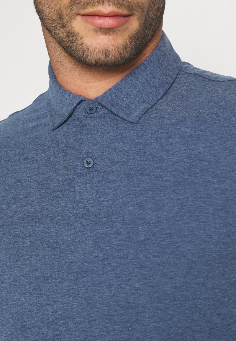 Polo en azul marino hecho de una tela texturizada con cuello clásico y cierre de dos botones, que presenta un sutil patrón jaspeado.