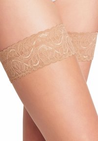 Nudefarget blonde strømper med blonder som går til lårene og har et delikat blomstermønster og bølget kant, kombinert med en glatt, lys hudtekstur.