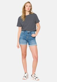 Črno-bele črtaste kratke majice, kombinirane z visokimi denim kratkimi hlačami. Model nosi bele superge z mornarsko modrim pridihom. Enostavna ozadja.