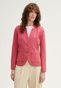 Blazer texturé rose avec un col cranté, deux poches avant et deux boutons, associé à un pantalon large crème.