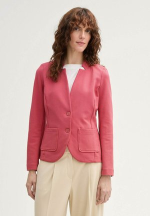 Blazer texturé rose avec un col cranté, deux poches avant et deux boutons, associé à un pantalon large crème.