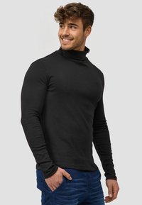Czarny longsleeve z golfem, wykonany z miękkiego materiału, o dopasowanym kroju i subtelnym logo na piersi. Połączony z niebieskimi dżinsami.
