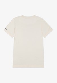 T-shirt en coton beige clair avec des manches courtes, col rond, arborant un petit logo marine sur la manche gauche. Texture lisse, design simple.