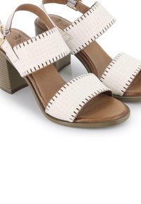 Sandalias de cuero trenzado beige con tacón cuadrado. Presentan dos correas anchas, detalles de costura y una planta de color marrón suave.