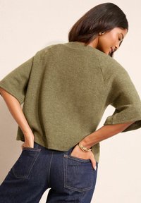 Olive rohelise värvi kudum, lühikeste varrukatega, lõdva lõikega ja tekstuurse materjaliga. Kombineeritud tumedate denimitehnika pükstega, millel on tavalised taskud.