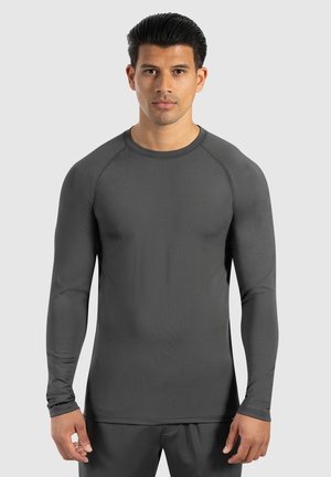Camiseta deportiva de manga larga en gris oscuro, hecha de un tejido suave y elástico. Presenta un cuello redondo y mangas raglán para mayor libertad de movimiento.