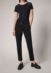 Top negro de manga corta con paneles de hombro brillantes, combinado con pantalones negros con cordón y cremalleras laterales. Mocasines de plataforma negros completan el look.