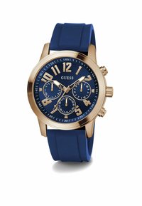 Orologio Guess con cinturino in silicone blu navy, cassa dorata e quadrante blu navy con grandi numeri arabi e sub-quadranti per data e ora.