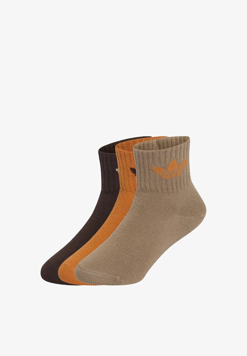 Trois chaussettes côtelées longueur cheville, en marron, orange et beige, chacune avec un petit logo près du bord.