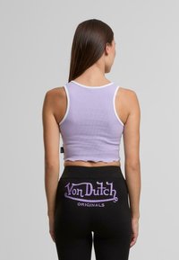 Ljuslila ribbat crop top med vit kant, har en vågig nederkant. Bärs med svarta leggings med lila "Von Dutch Originals"-text.