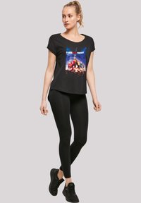 Svart kortermet t-skjorte med et fargerikt grafisk trykk fra "The Big Bang Theory", kombinert med svarte leggings og svarte sneakers.