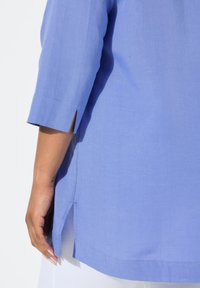 Blusa in lino blu con maniche a tre quarti, fessure laterali e orlo dritto, che mette in mostra una texture liscia e una finitura pulita.