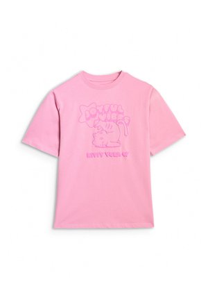 Młoda dziewczyna stoi, ubrana w różowy oversize T-shirt z grafiką kota i szare szerokie spodnie na białym tle.
