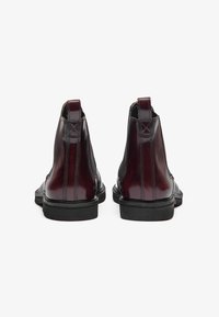 Botine din piele bordeaux cu panouri elastice pe laterale, talpă din cauciuc mată neagră și o bucată de prindere la spate pentru a facilita încălțarea.